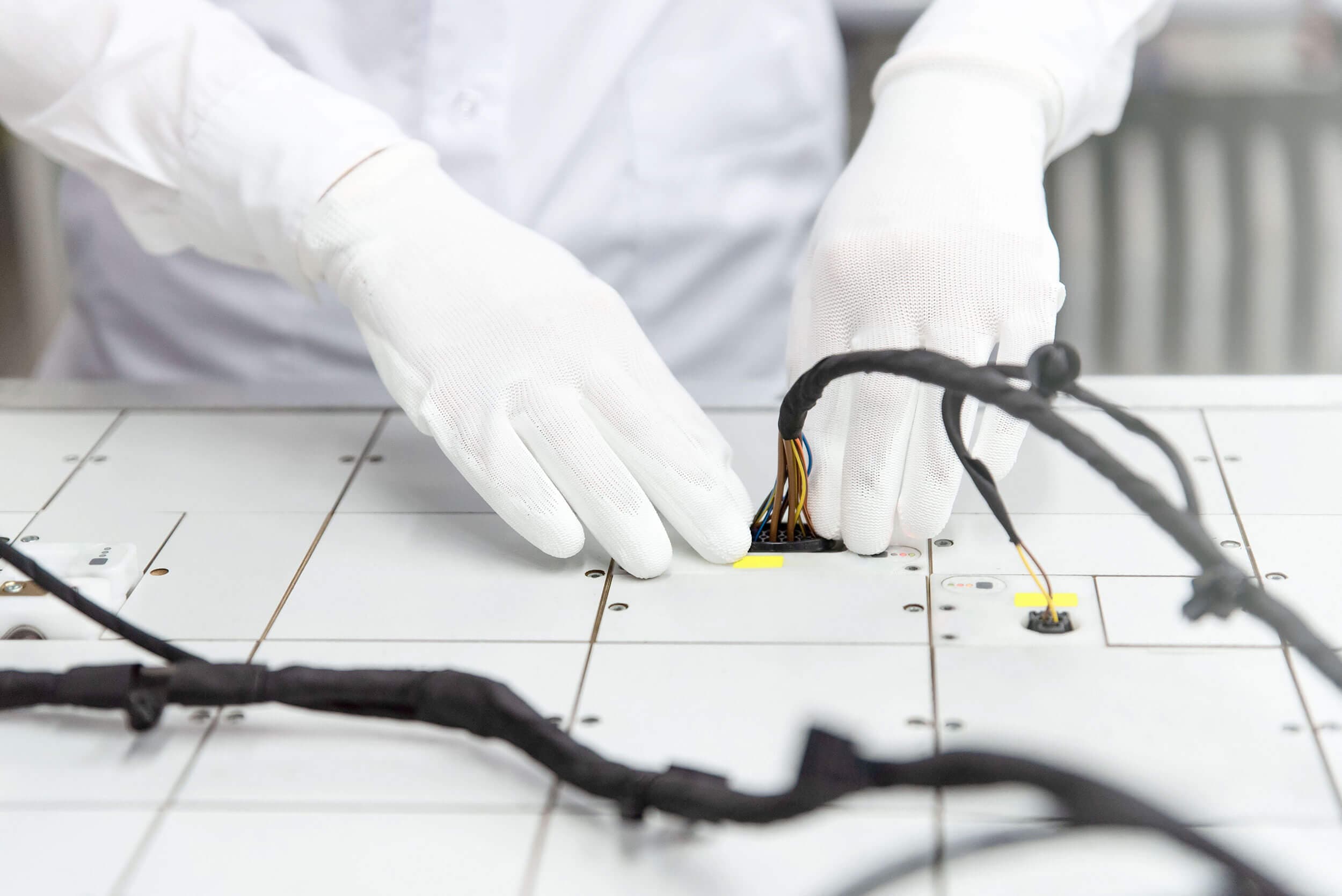 Employees in white gloves assembling a wiring harness
